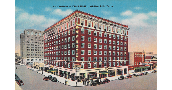 A color postcard of a multi-story red brick hotel building on a street corner.