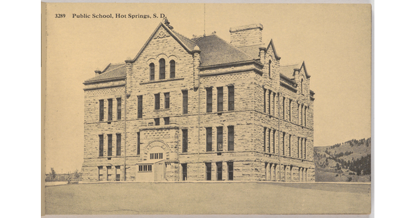 A sepia-toned photograph of a four-story stone building on a grassy lawn with the label "Public School, Hot Springs. S.D."