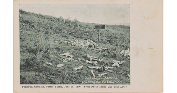 A black-and-white photograph of a field with human bones scattered everywhere and a wooden sign that reads, "UNKNOWN."