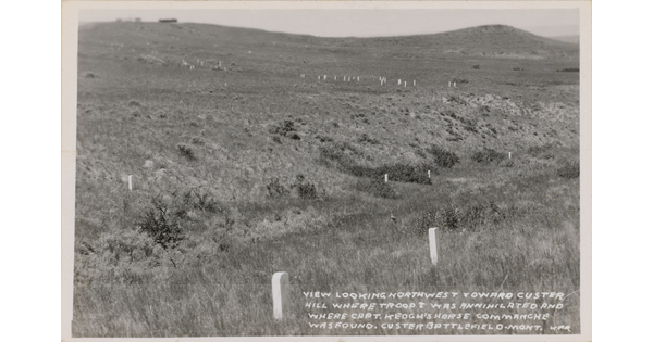 A black-and-white photograph postcard of grassy hills and scattered grave markers.