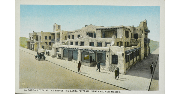 A color postcard of a multi-story adobe hotel with people walking on the sidewalks next to it.