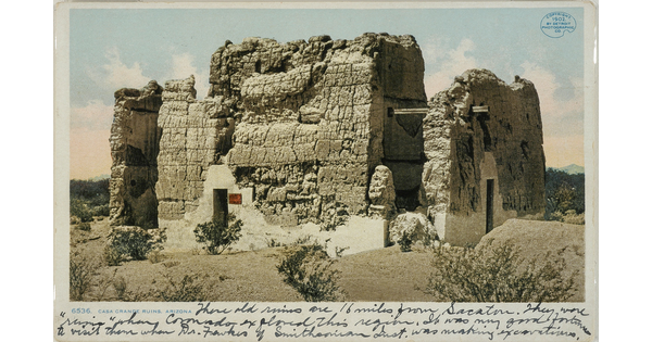 A color postcard of a ruined adobe building in a desert landscape with black cursive handwriting along the bottom edge of the postcard.