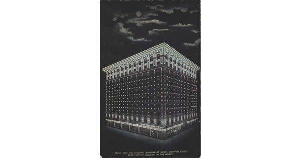 A color postcard of a nine-story building lit up at night under a full moon that is partially hidden behind clouds.