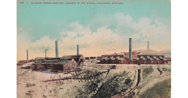 A color postcard of several industrial brick buildings with smokestacks in a mostly dirt terrain.