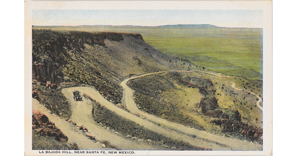 A color postcard of a high mesa with a car driving on a road that zig-zags back and forth down its side.