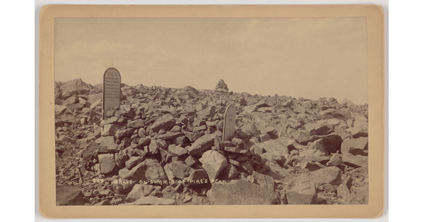 A sepia-toned photograph of two gravestones surrounded by large rocks.