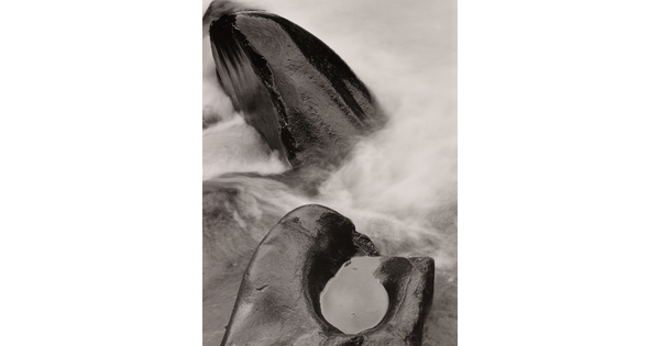 A black-and-white photograph of steam rising from two rocks, one with a pool of water in it.