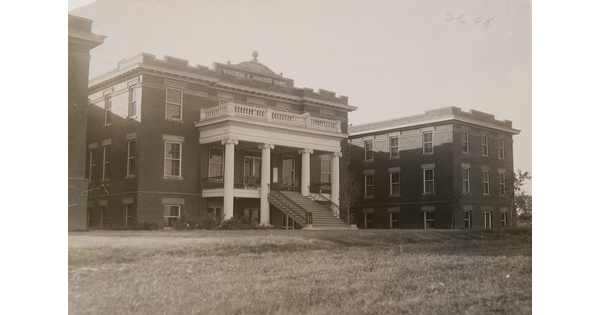 A black-and-white photograph of a three-story building with a large staircase that leads to a columned entrance.