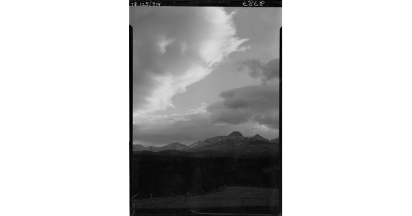 A black-and-white image of a dark mountain landscape under a cloudy sky.