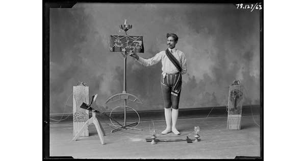 A black-and-white image of a man standing in front of a sign that reads, "The Great Layton," and other performance props.