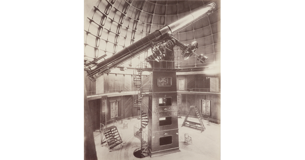 A sepia-toned photograph of a large telescope inside of a domed structure.