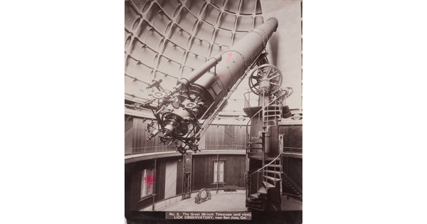A sepia-toned photograph of a large telescope with complex gears on the end sitting atop a spiral staircase inside a domed structure.