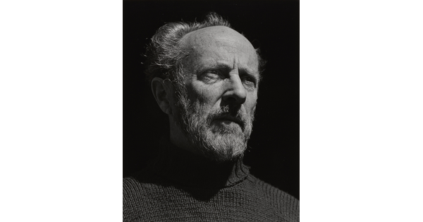 A black-and-white portrait photograph of an older, bearded White man wearing a turtleneck looking out into the distance.