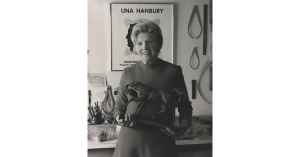 A black-and-white portrait of an older, White woman holding a horse sculpture in a studio.