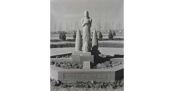 A black-and-white photograph of a stone statue of a stylized figure standing between stylized stone trees.