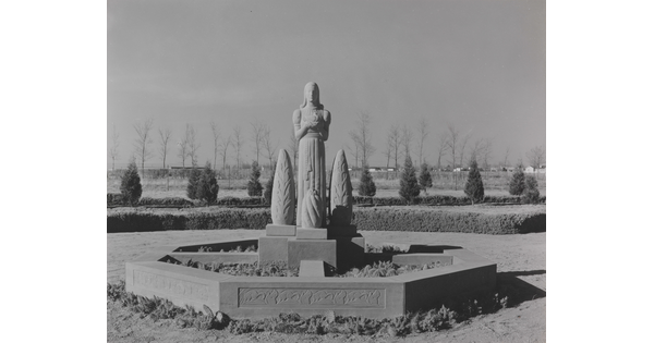 A black-and-white photograph of a stone statue of a stylized figure standing between stylized stone trees.