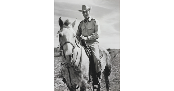 A black-and-white photograph of a White man in a cowboy hat sitting astride a dappled horse.