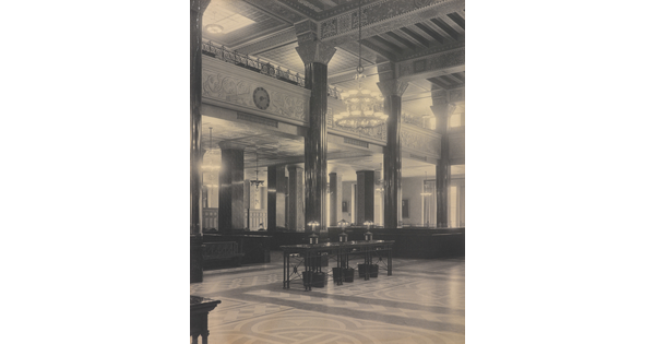 A black-and-white photograph of the interior of an ornate office lobby with inlaid floors, columns, and chandeliers.