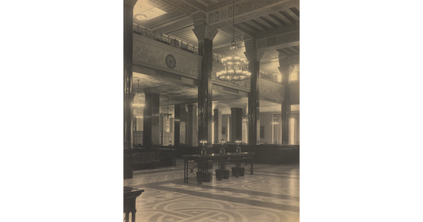 A black-and-white photograph of the interior of an ornate office lobby with inlaid floors, columns, and chandeliers.