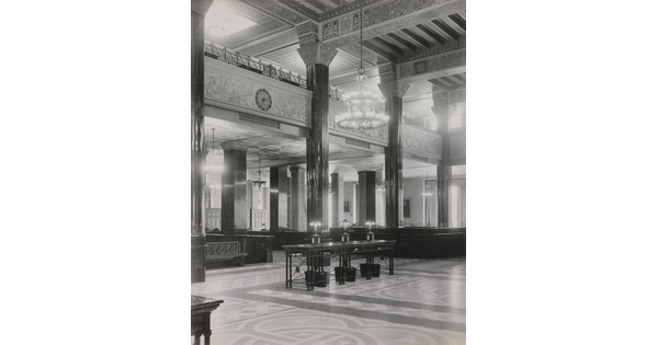 A black-and-white photograph of the interior of an ornate office lobby with inlaid floors, columns, and chandeliers.