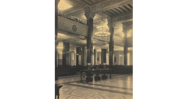 A black-and-white photograph of the interior of an ornate office lobby with inlaid floors, columns, and chandeliers.