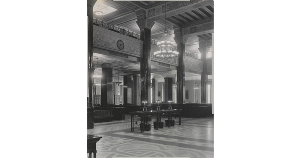 A black-and-white photograph of the interior of an ornate office lobby with inlaid floors, columns, and chandeliers.