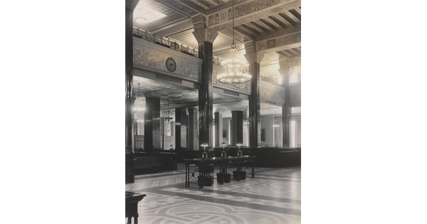 A black-and-white photograph of the interior of an ornate office lobby with inlaid floors, columns, and chandeliers.