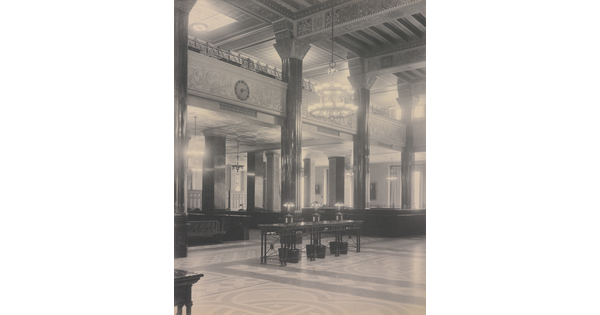 A black-and-white photograph of the interior of an ornate office lobby with inlaid floors, columns, and chandeliers.