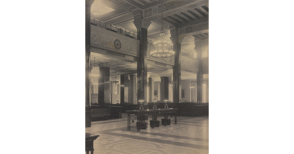 A black-and-white photograph of the interior of an ornate office lobby with inlaid floors, columns, and chandeliers.