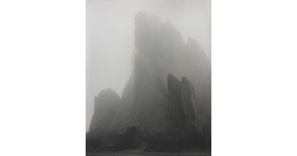 A black-and-white photograph of a large rock formation partially hidden by fog.