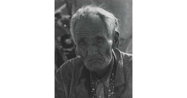 A black-and-white portrait photograph of an elderly Indigenous man with deep wrinkles and sunken cheeks.