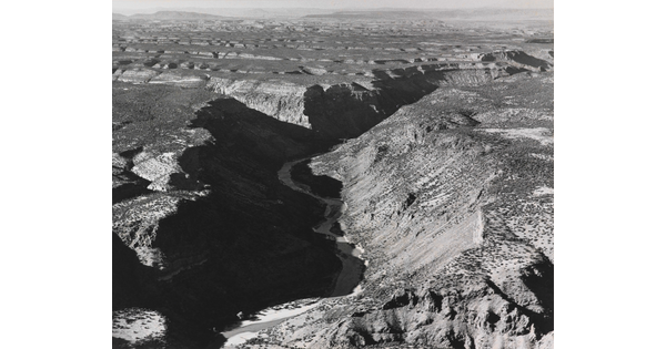 A black-and-white photograph of an aerial view of a river winding through a steep canyon.