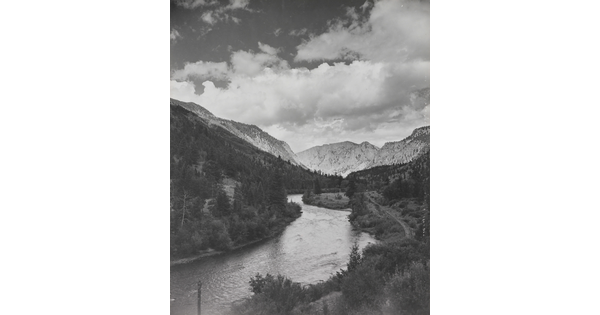 A black-and-white photograph of a river winding through a mountain valley under a cloudy sky.