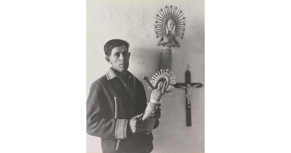 A black-and-white photograph of a medium-skinned man in a winter jacket holding an elaborately carved wooden figure.