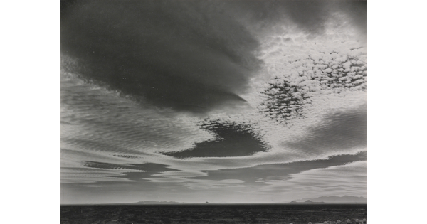 A black-and-white photograph of an expansive desert plain under rippled clouds with mountains in the far distance.