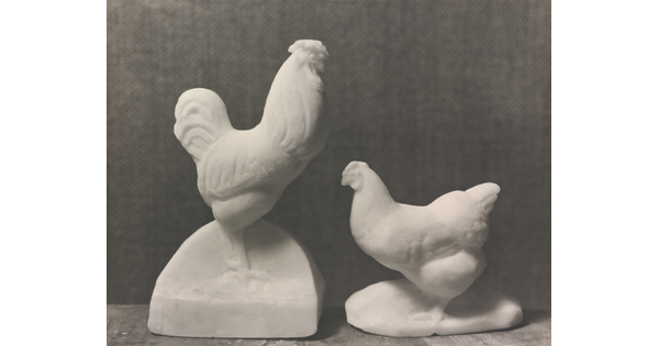 A black-and-white photograph of sculptures of a rooster and hen carved out of white soap.