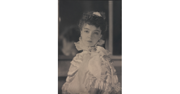 A black-and-white portrait photograph of a White woman with curly hair pulled on top of her head, wearing a top with a ruffled collar.