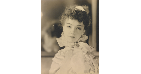 A black-and-white portrait photograph of a White woman with curly hair pulled on top of her head, wearing a top with a ruffled collar.