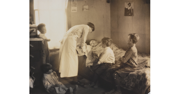 A black-and-white photograph of a nurse bending over a person in a bed, two children sitting on the bed, and two children behind the nurse.