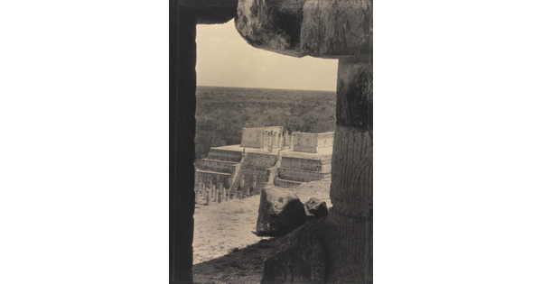 A sepia-toned photograph of an ancient step pyramid viewed through a stone window.