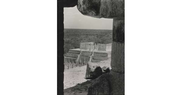 A black-and-white photograph of an ancient step pyramid viewed through a stone window.