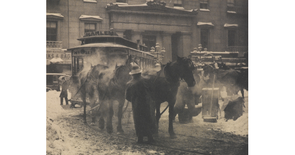 A black-and-white photograph of horses pulling a trolley on a busy street covered with slush and snow.