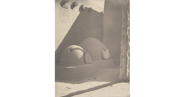 A black-and-white photograph of two beehive ovens attached to an adobe structure.