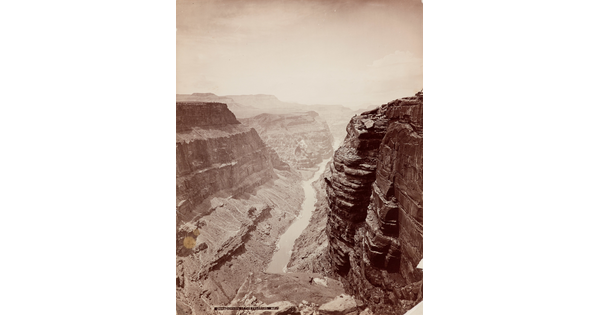 A sepia-toned photograph of a river at the bottom of a steep canyon with sheer cliffs on both sides.