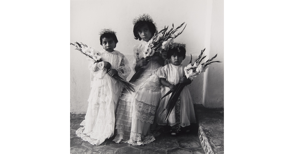 A black-and-white photograph of three young medium-skinned girls wearing floral tiaras, light-colored dresses, and holding bouquets of lilies.