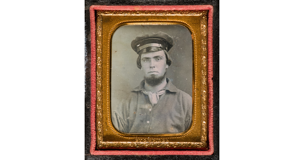 A black-and-white photograph in a gold frame and case of a young man posed in a military hat.