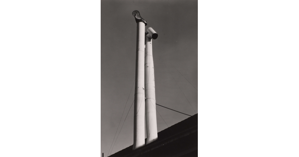 A black-and-white photograph looking up at two tall white pipes jutting out from the roof of a building.