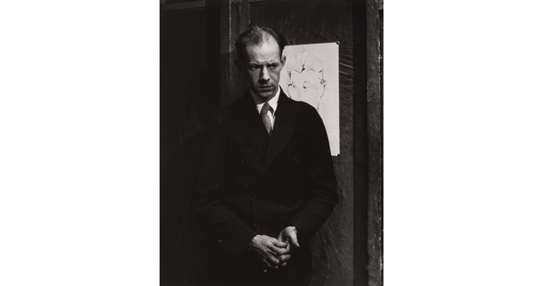 A black-and-white portrait photograph of a balding White man wearing a coat and tie holding his hands clasped in front of him.