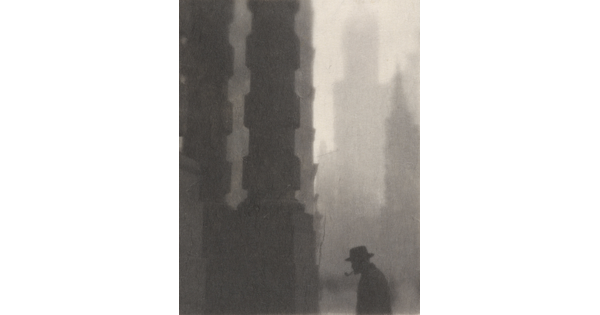 A black-and-white photograph of the silhouette of a man smoking a pipe next to towering columns and buildings.