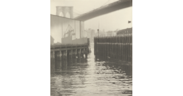 A black-and-white photograph of the shadow of a ship on top of a pier in a busy harbor.
